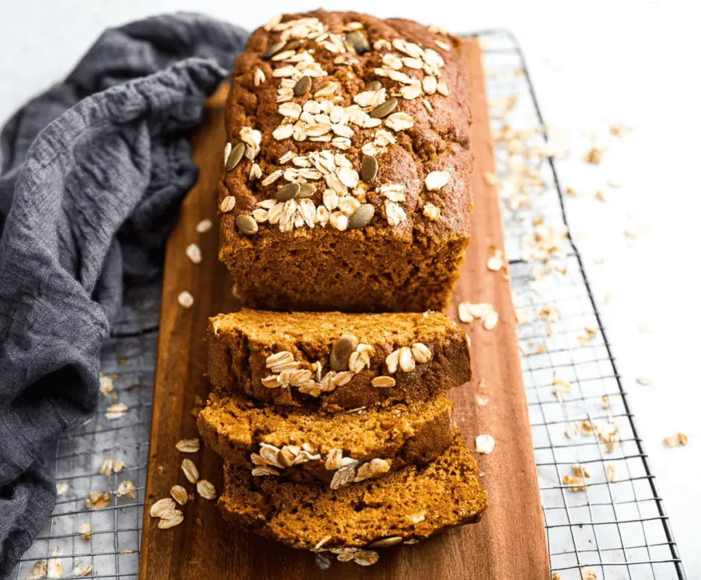 Delicious homemade pumpkin oatmeal bread sliced and ready to serve on a rustic wooden table, featuring a golden-brown crust and moist pumpkin-flavored interior