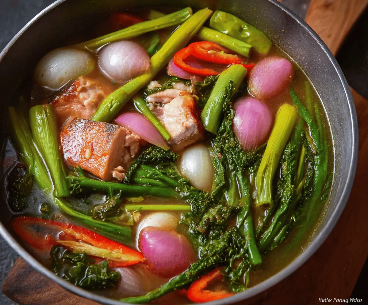A steaming bowl of traditional Sinigang soup with tender pork, fresh vegetables, and tangy tamarind broth, served with rice on the side.