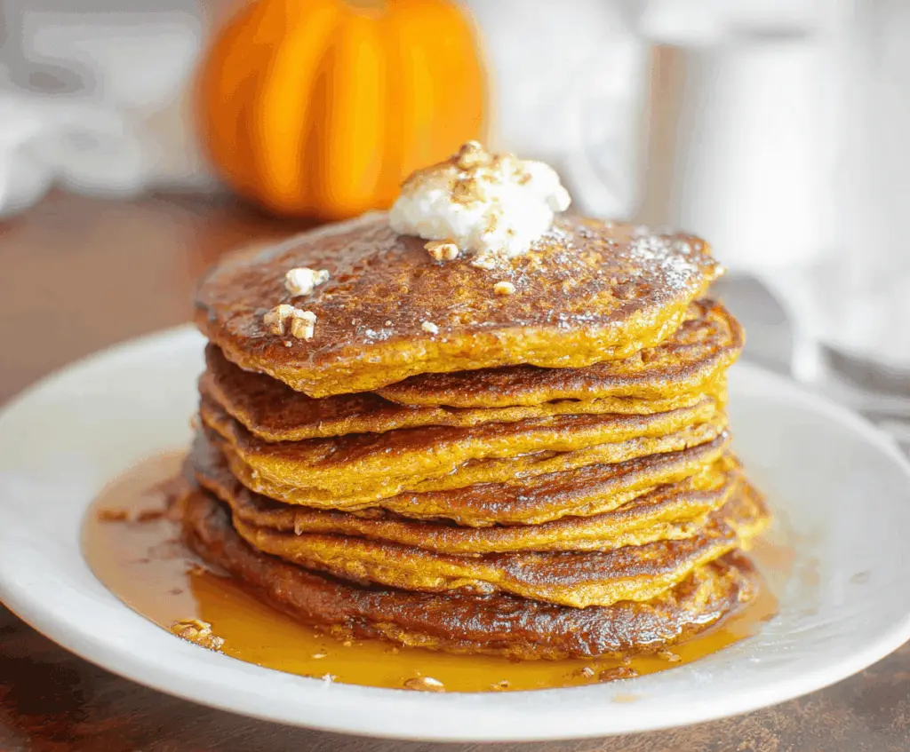 Delicious homemade sourdough pumpkin pancakes topped with fresh maple syrup and chopped pecans on a rustic plate