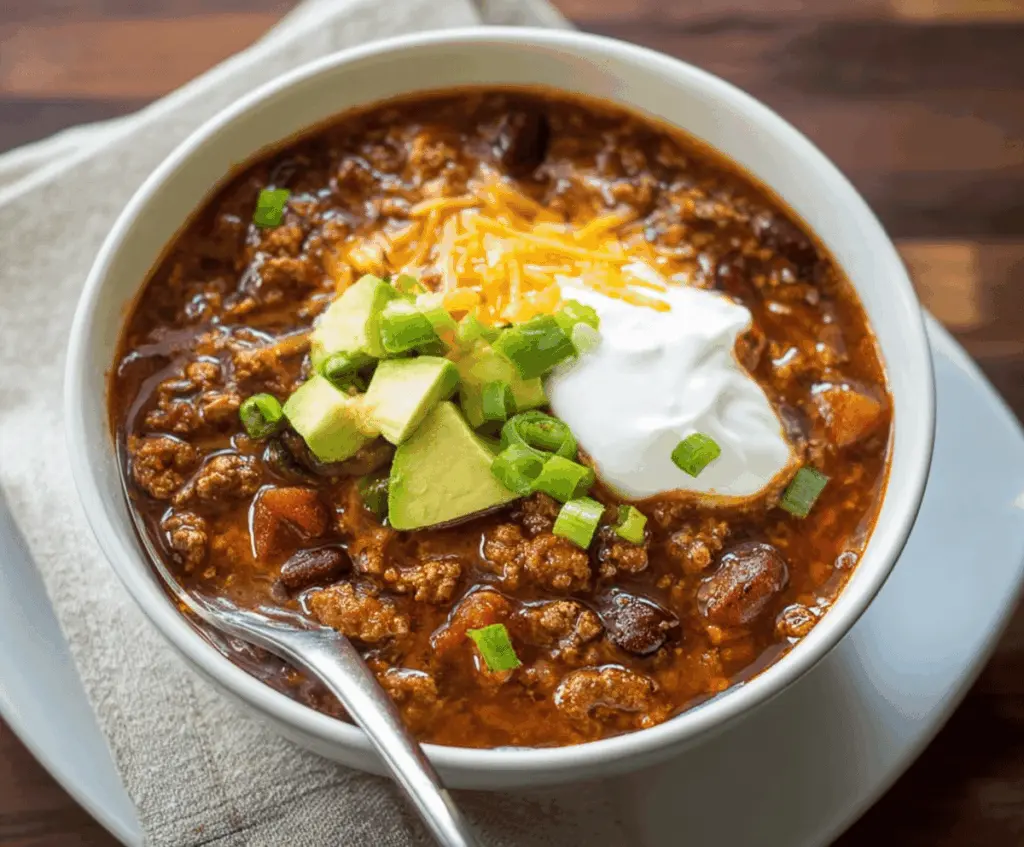 Hearty venison chili topped with shredded cheese and fresh herbs in a rustic bowl, perfect for a comforting meal.