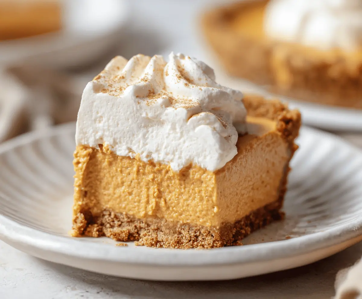 Delicious Pumpkin Cool Whip Pie topped with whipped cream and cinnamon, served on a white plate for a fall dessert.