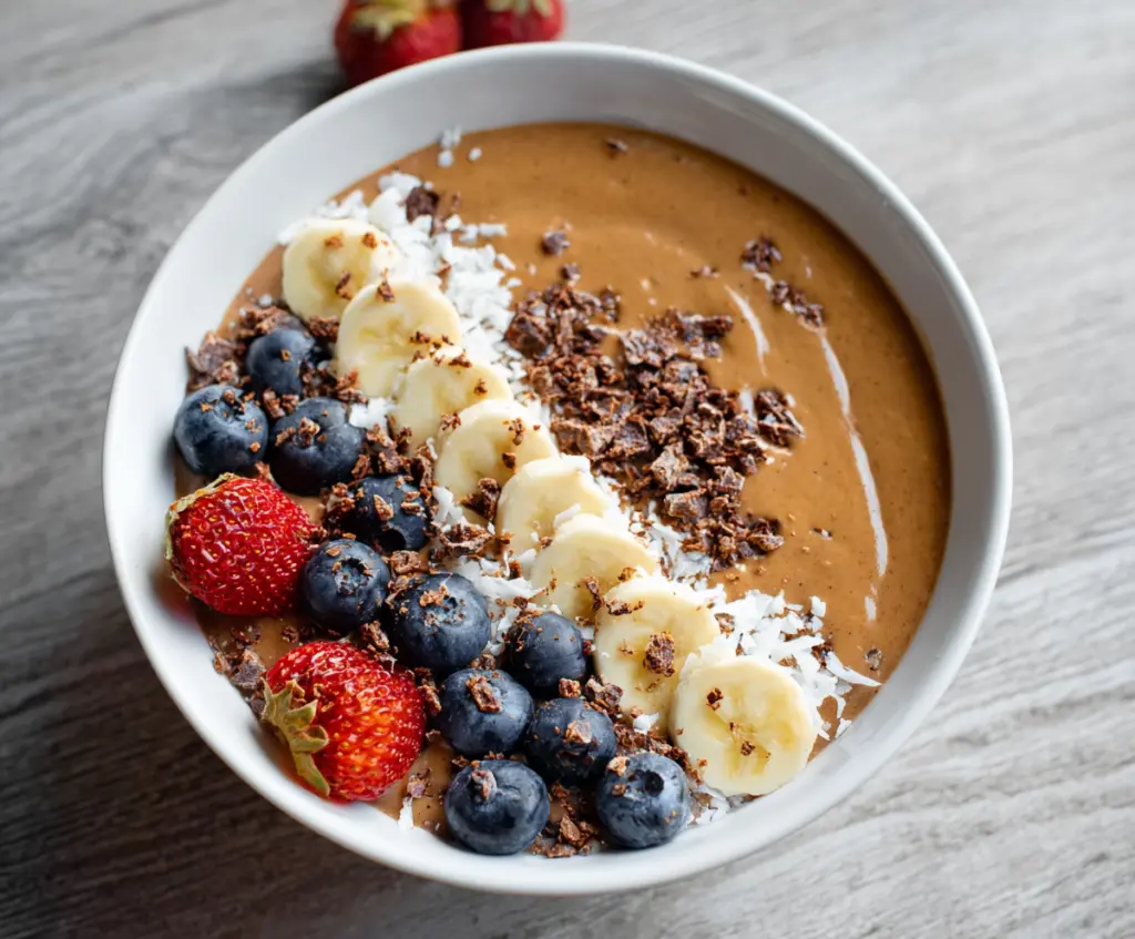 Colorful protein smoothie bowl topped with fresh berries, sliced bananas, and granola, served in a white bowl for a healthy breakfast.