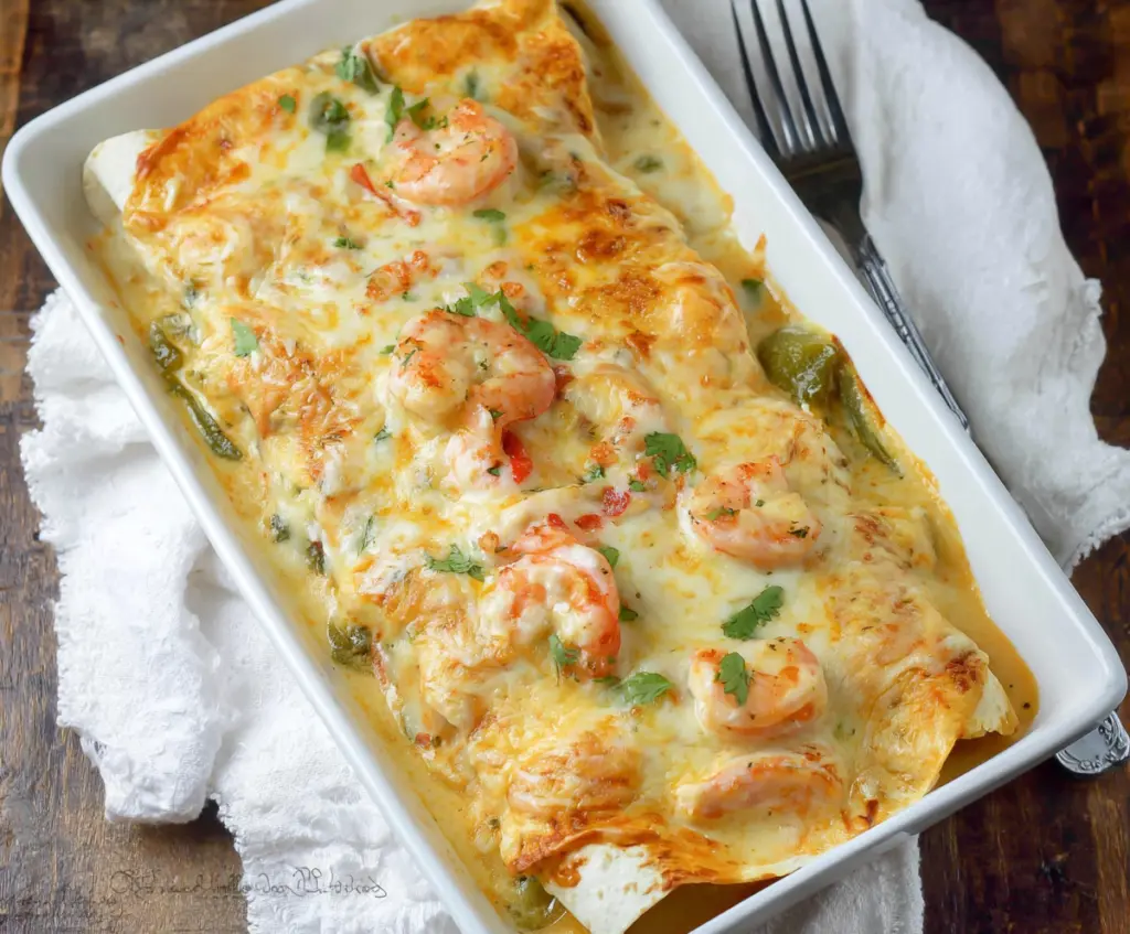 Delicious creamy shrimp enchiladas served on a plate with melted cheese and fresh herbs.