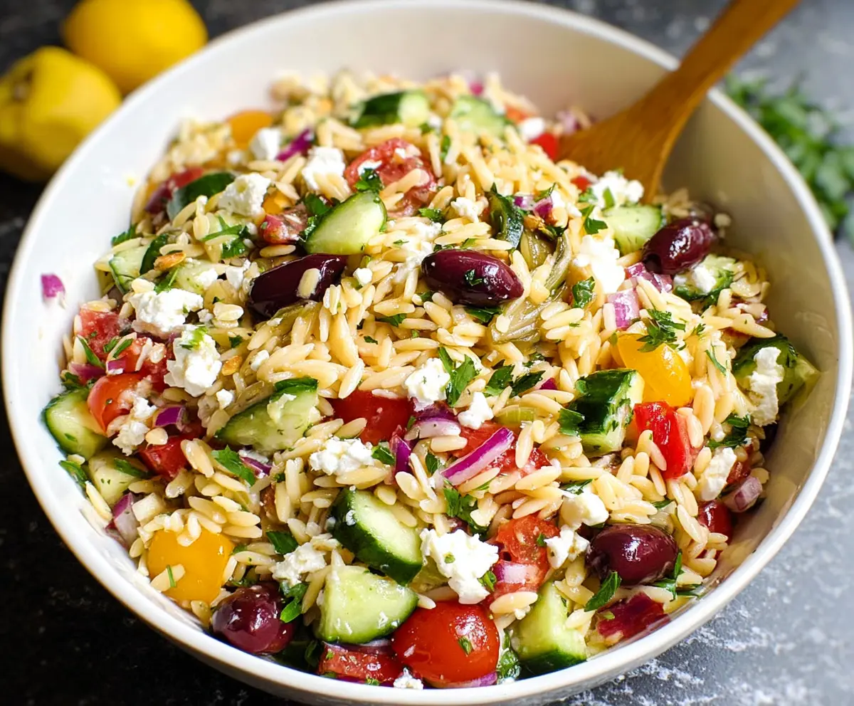 Fresh Greek Orzo Salad with cherry tomatoes, feta cheese, cucumbers, and herbs in a bowl.